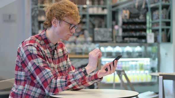 Attractive Young Redhead Man Using Smartphone in Cafe
