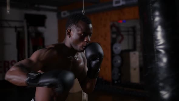 Africanamerican Athletic Halfnaked Young Man Boxer Training on the Punching Bag in the Gym