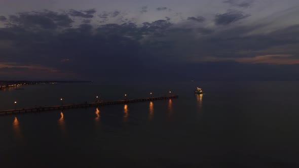 Flying over sea, pier and sailing boat at night