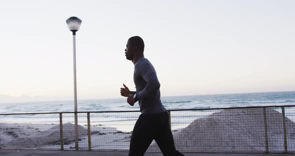 Focused african american man exercising outdoors, running by seaside