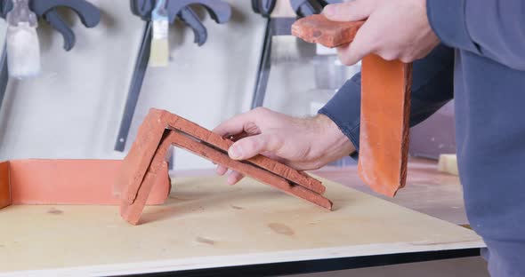 Worker Puts Decorative Orange Bricks on Table at Workshop