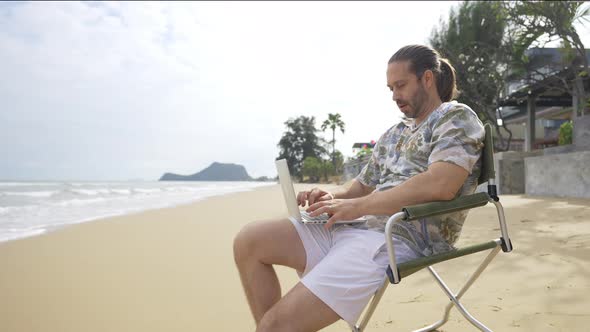 4K Caucasian businessman sitting on outdoor chair and working on laptop computer at the beach.