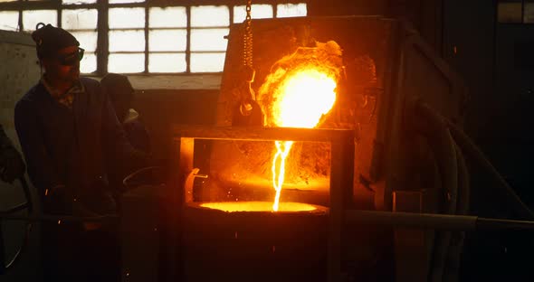 Worker pouring molten metal from container in foundry workshop 4k