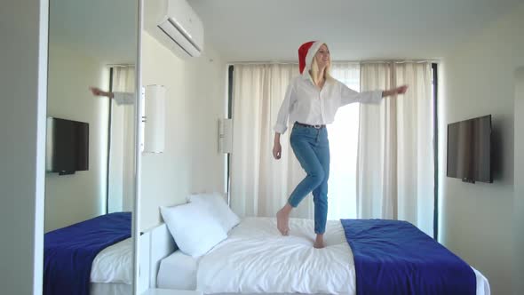 slender beautiful girl dancing in a Santa Claus hat on the bed.