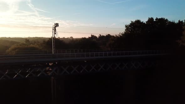 Horizontal aerial following & ascending over railway bridge sunrise, early, frosty, misty morning