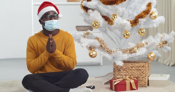 Webcam View African Black Man Guy in New Year's Suit Sits Near Christmas Tree Wears Medical Mask on