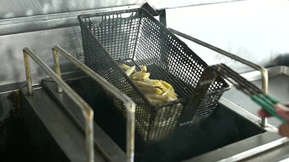 Crop cook preparing French fries in deep fryer in kitchen