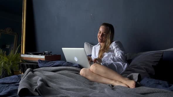 Woman in Headphones Sit on Bed at Home Wave Greet Hand Talk on Video Call on Laptop