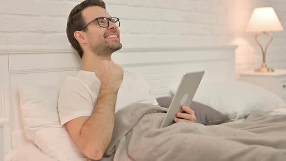Excited Young Man Celebrating on Tablet in Bed
