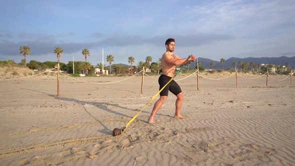 muscular athlete training functional exercises performs dragging on the beach with weight