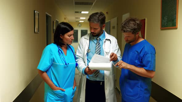 Doctor interacting over a report with ward boy and nurse in corridor