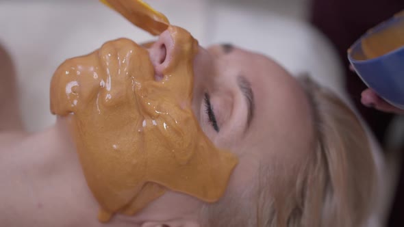 Closeup Beautician Applying Yellow Facial Mask on Lower Face of Client in Beauty Spa