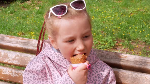 Pretty little girl eating an ice cream in waffle cone on bench outdoor Child in sunglasses in park