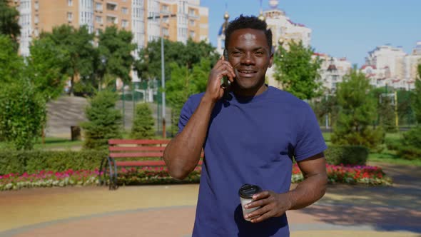Smiling AfroAmerican Man Talking on Mobile Phone Holding Paper Cup for Coffee