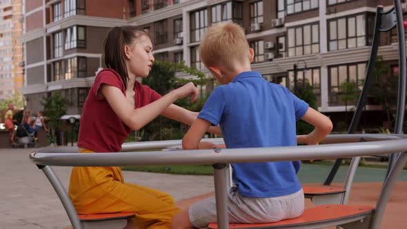 A Brother and Sister are Having Fun Riding on a Carousel in the Courtyard