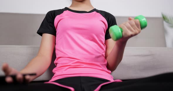 Woman holding smartphone and training dumbbells