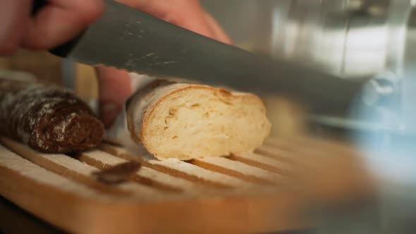 Slicing French Baguette with Knife on Wooden Board for Bread.