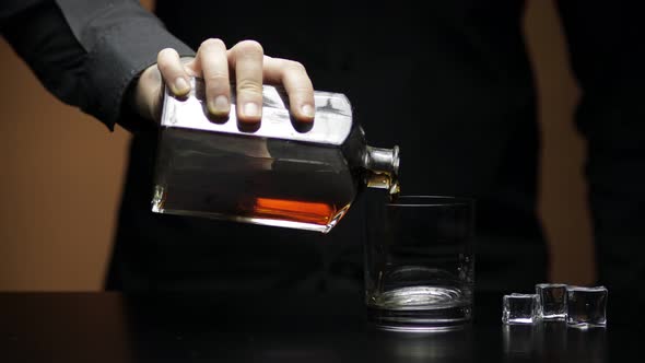 Pouring Whiskey, Cognac Into Glass with Ice Cubes. Bartender Pours Alcohol Drink