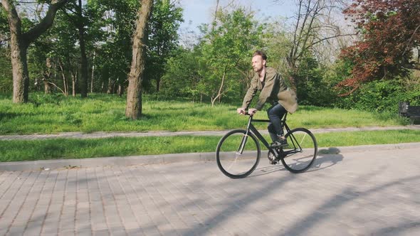 Tracking Shot of Hipster Man Riding Fixed Gear Bicycle in Park Slow Motion