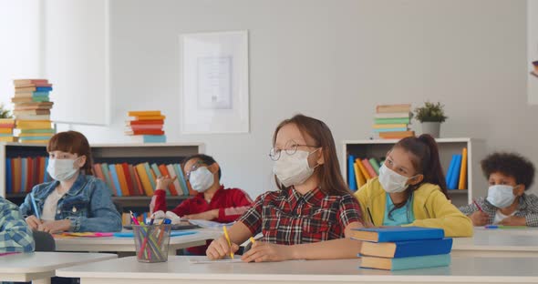 Diverse Children Raising Hands for Answer Wearing Medical Masks for Protection From Virus at Lesson