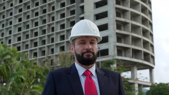 Portrait of a Design Engineer in a White Protective Helmet in a Business Suit with a Red Tie Against