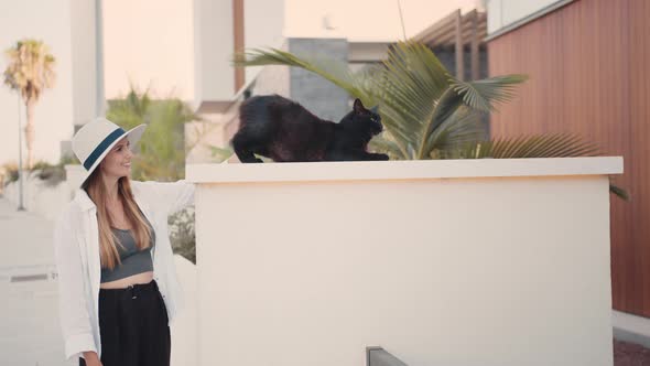 Happy Caucasian Woman Petting Black Cat That Sunbathing on City Street