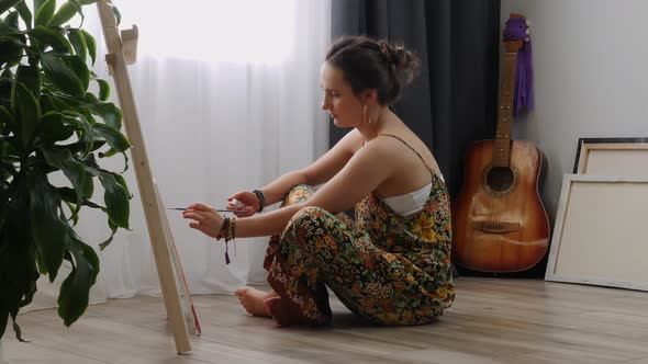 Young woman drawing picture on canvas at home in sunny day