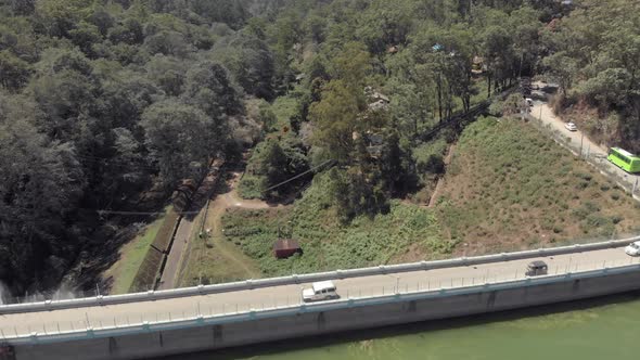 Cars driving across barrage dam, Munnar, India.  Aerial backward 