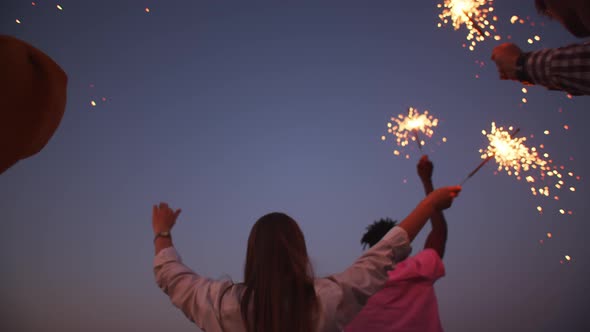 International friends in the evening in nature held lighted sparklers their hands background the sky