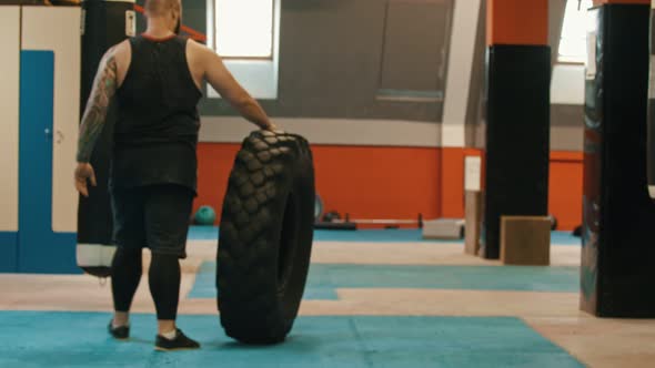 A Man Bodybuilder Rolls a Big Tire in the Gym