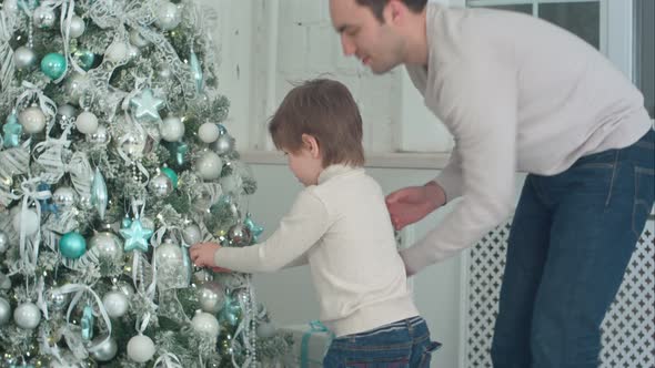 Father and Son Decorating Christmas Tree with Baubles in the Living Room
