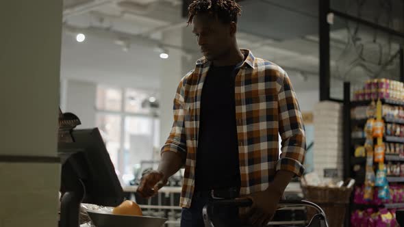 Man with Shopping Trolley Weighing Fruits on the Scales in the Supermarket