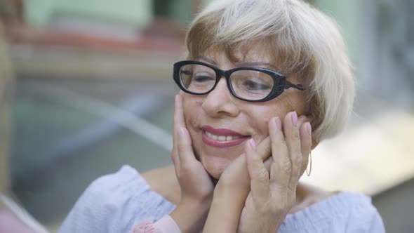 Close-up of Happy Caucasian Senior Woman in Eyeglasses with Unrecognizable Little Girl Holding Her