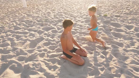 Happy Little Boy Running Around the White Sand Beach Is About a Teenage Brother in the Setting Sun