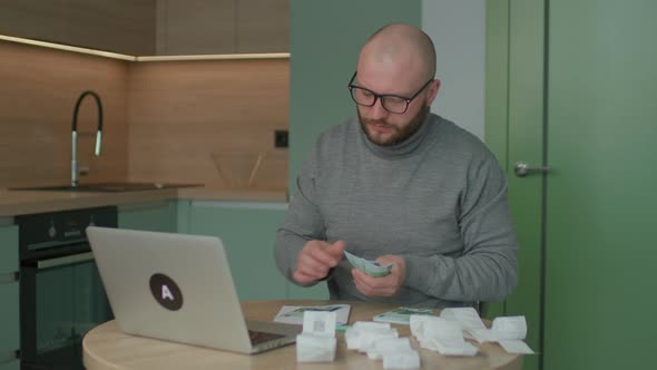 30s Man Counting Euros for Home Budget with Store Receipts on the Table