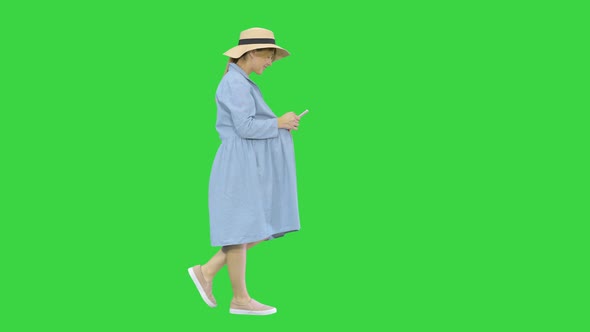 Young Pregnant Woman in Trendy Hat Walking and Using Her Phone on a Green Screen, Chroma Key.