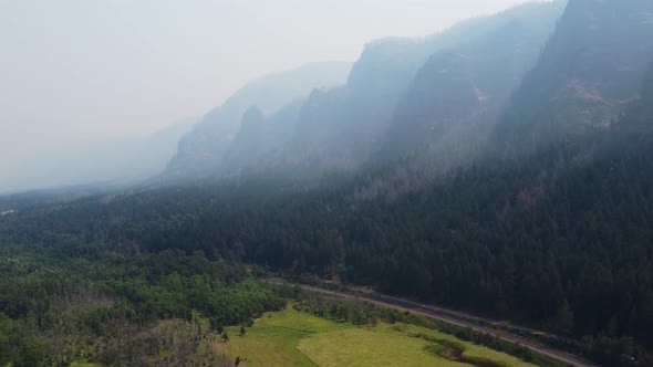 Drone shot of towering mountains masked by smoke and contrasted by greenery in the Columbia River Go