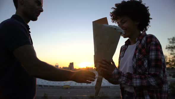 Man Presenting Bouquet of White Flowers to Biracial Girlfriend at Outdoor Date