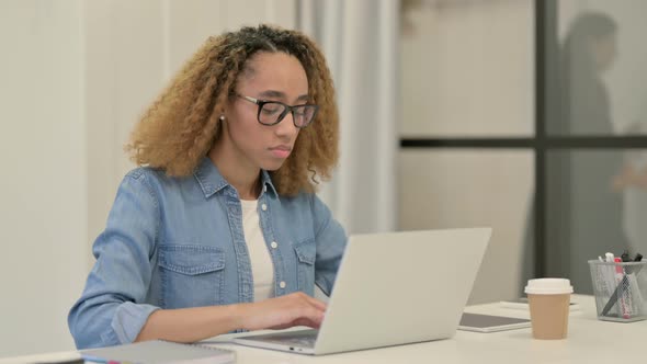 African Woman Looking at Camera While Working on Laptop