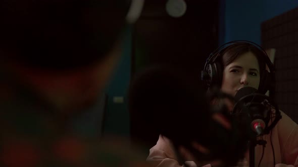 Young woman talking in mic while recording podcast with crop coworker