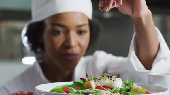 African american female chef garnishing dish and similing in restaurant kitchen