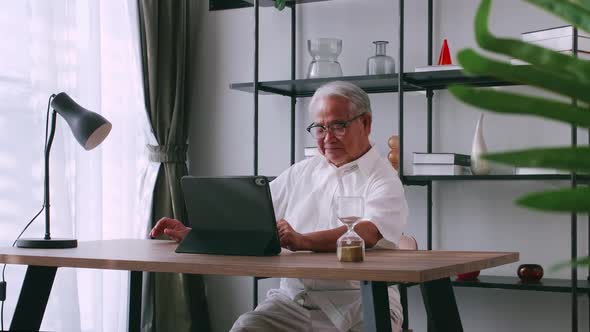 An old Asian man is searching for information on the Internet while sitting at a table.