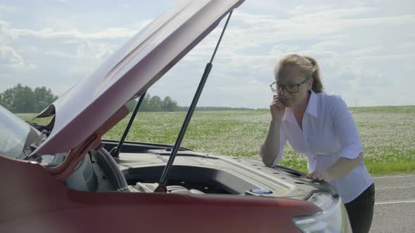 Woman looks under the hood of a Car.