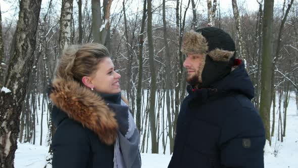 Happy Couple Woman Puts Scarf on Frozen Guy in the Snowcovered Winter Forest