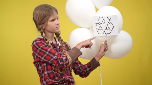 Serious Girl Pointing at Recycle Symbol on White Balloon Standing at Yellow Background