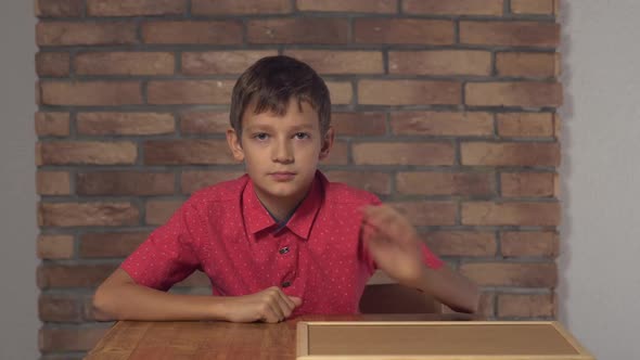 Child Sitting at the Desk Holding Flipchart with Lettering Boss on the Background Red Brick Wall