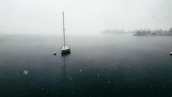 Snow falling over Maggiore lake and moored sailing boat and ferryboats, Italy. Panning