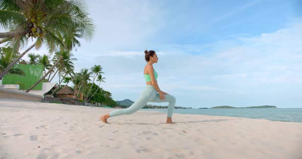 Young Brunette Sport Woman Makes Exercises on the Beach on Yoga Mat Dressed in Green Sportswear