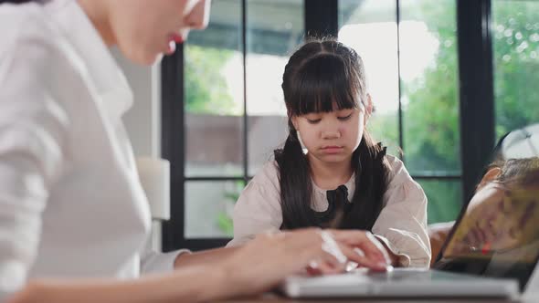 Asian kid feeling sad and need to play with her mom. The mother is busy on working on her job