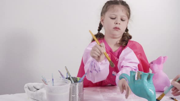 Little girl painting paper mache figurines with acrylic paint  for her homeschooling art project